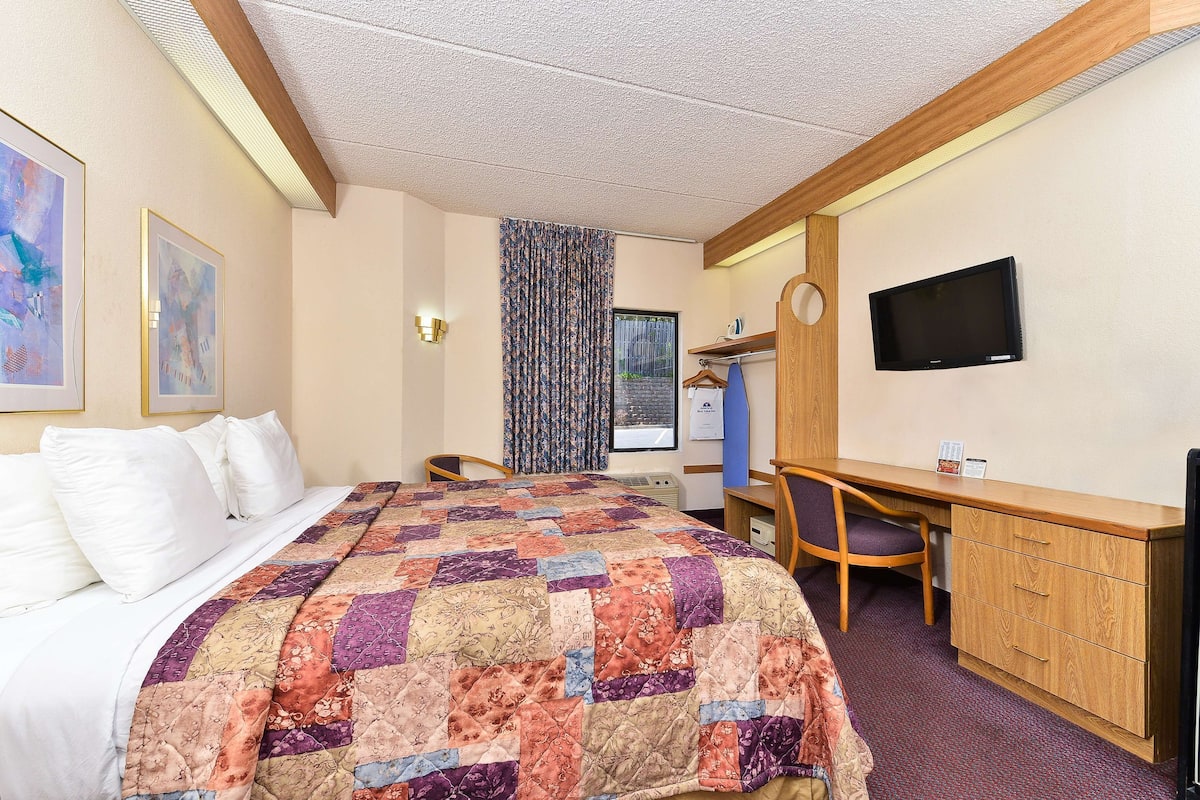 A hotel room with a bed, a desk, a chair, a television, and a window with curtains.