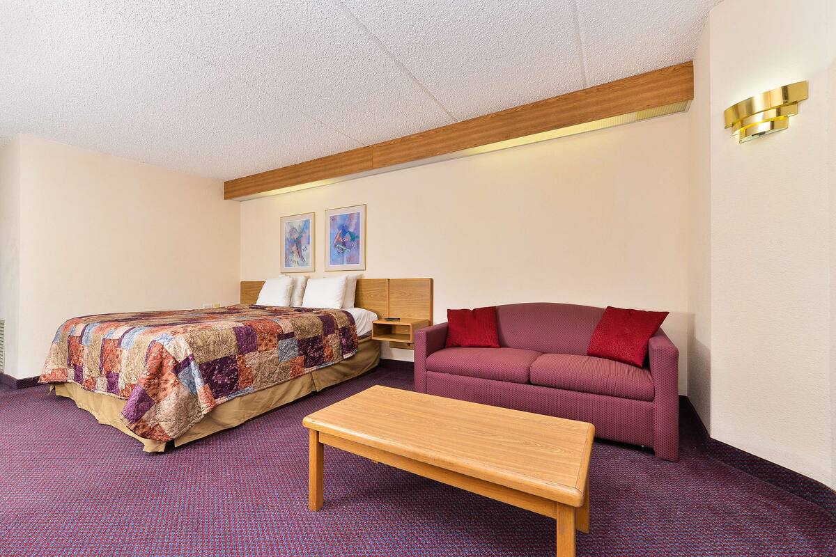 A hotel room with a bed, a red sofa, a wooden table, and two paintings on the wall.