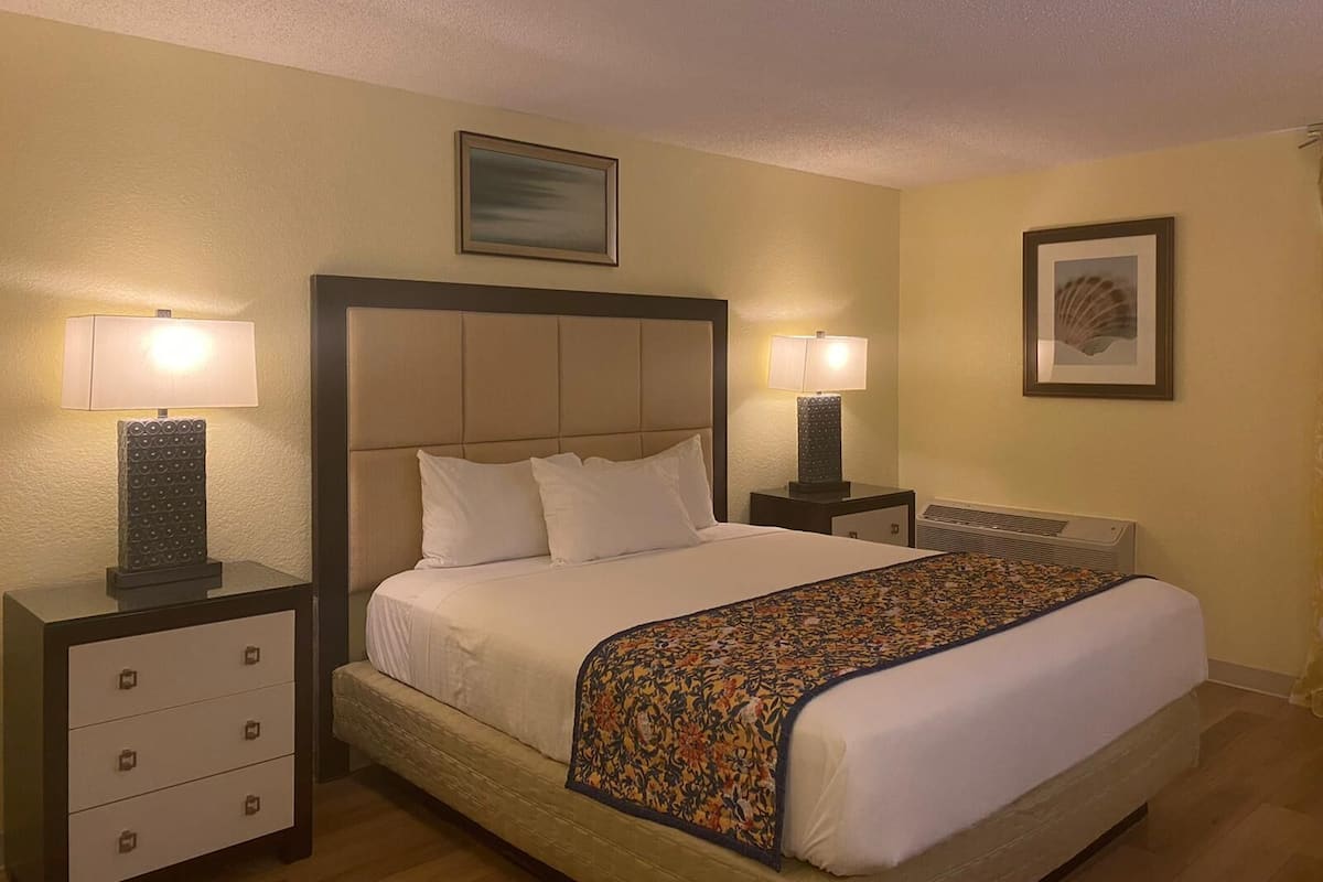 A hotel room with a large bed, two bedside tables with lamps, a framed picture above the bed, and a radiator on the wall.