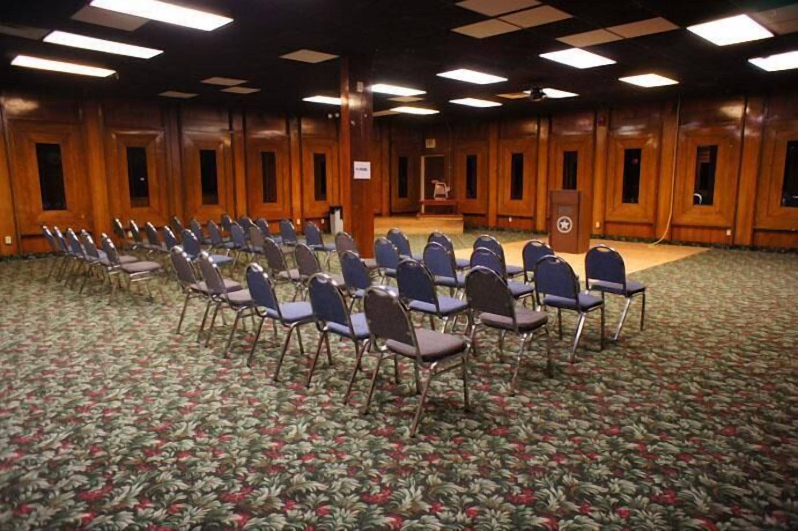 Une salle de conférence avec des rangées de chaises, un pupitre et un lambris en bois.