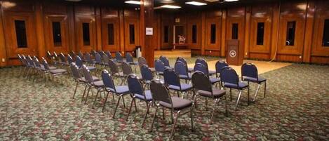 Uma sala de conferências com fileiras de cadeiras, um pódio e painéis de madeira.