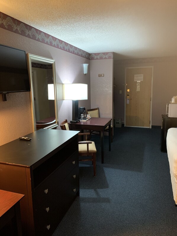 Una habitación de hotel con escritorio, silla, lámpara, televisión y cama.