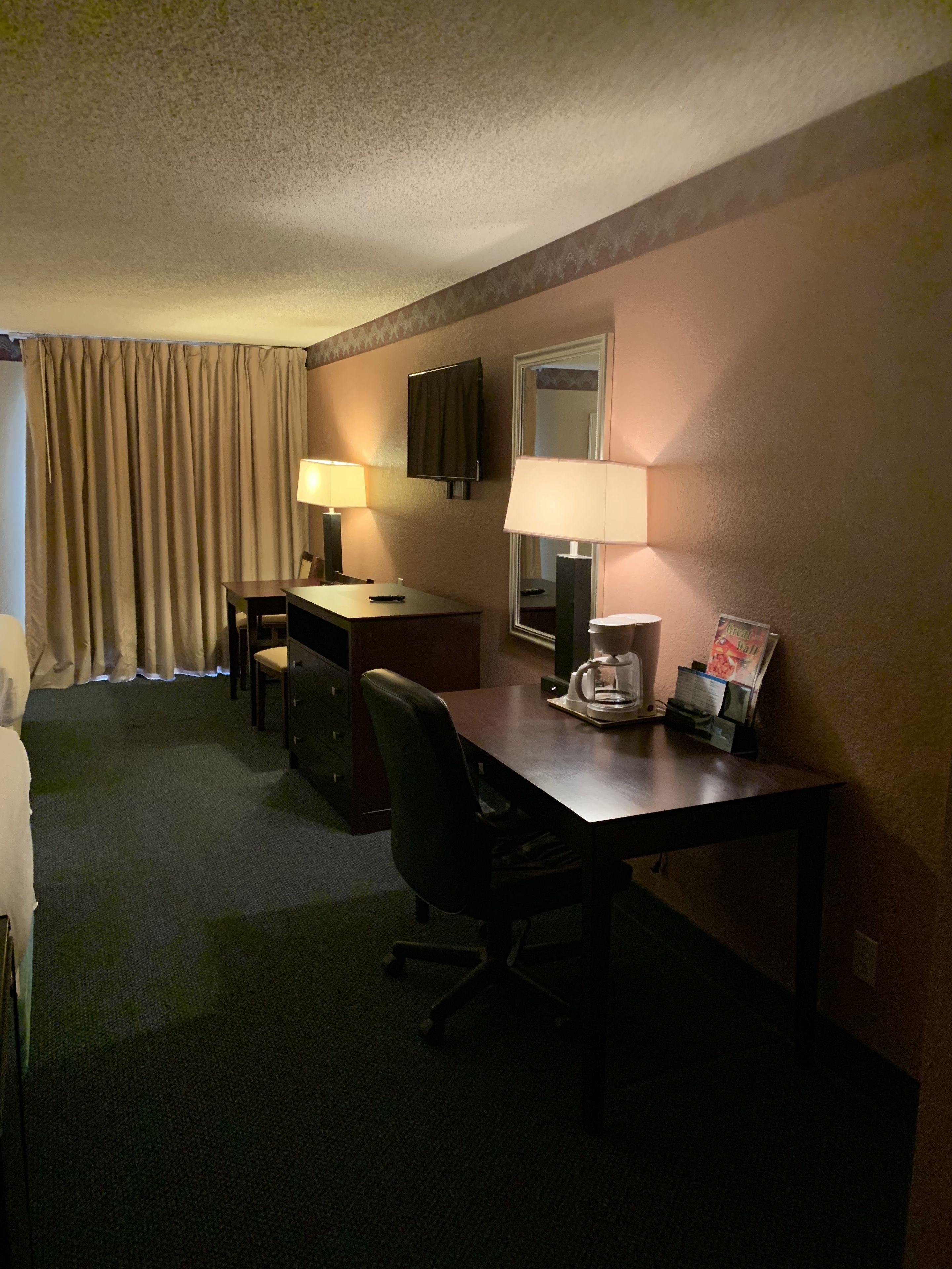 Une chambre d’hôtel équipée d’un bureau, de deux lampes, d’une chaise, d’une télévision et d’un miroir.