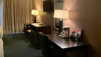 Habitación de hotel con escritorio, dos lámparas, una silla, televisor y espejo.
