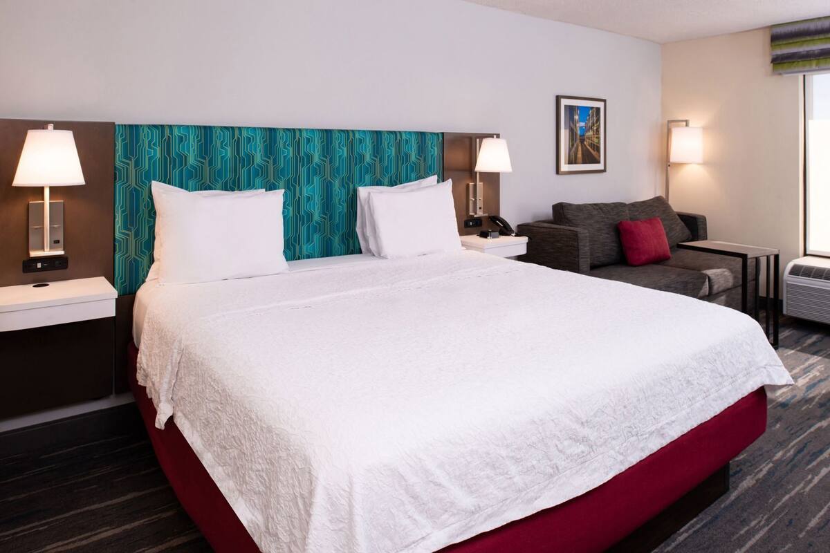 A hotel room with a large bed, two bedside tables, a sofa, and a wall-mounted TV.