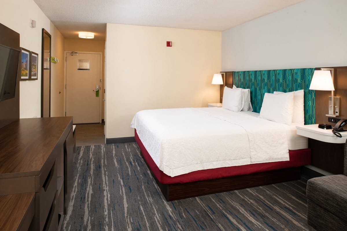 A hotel room with a bed, bedside tables, a desk, and a television.