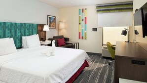 A hotel room with a large bed, a desk, a chair, a TV, and a wall-mounted air conditioner. - Hampton Inn Greensboro-Airport (Greensboro)
