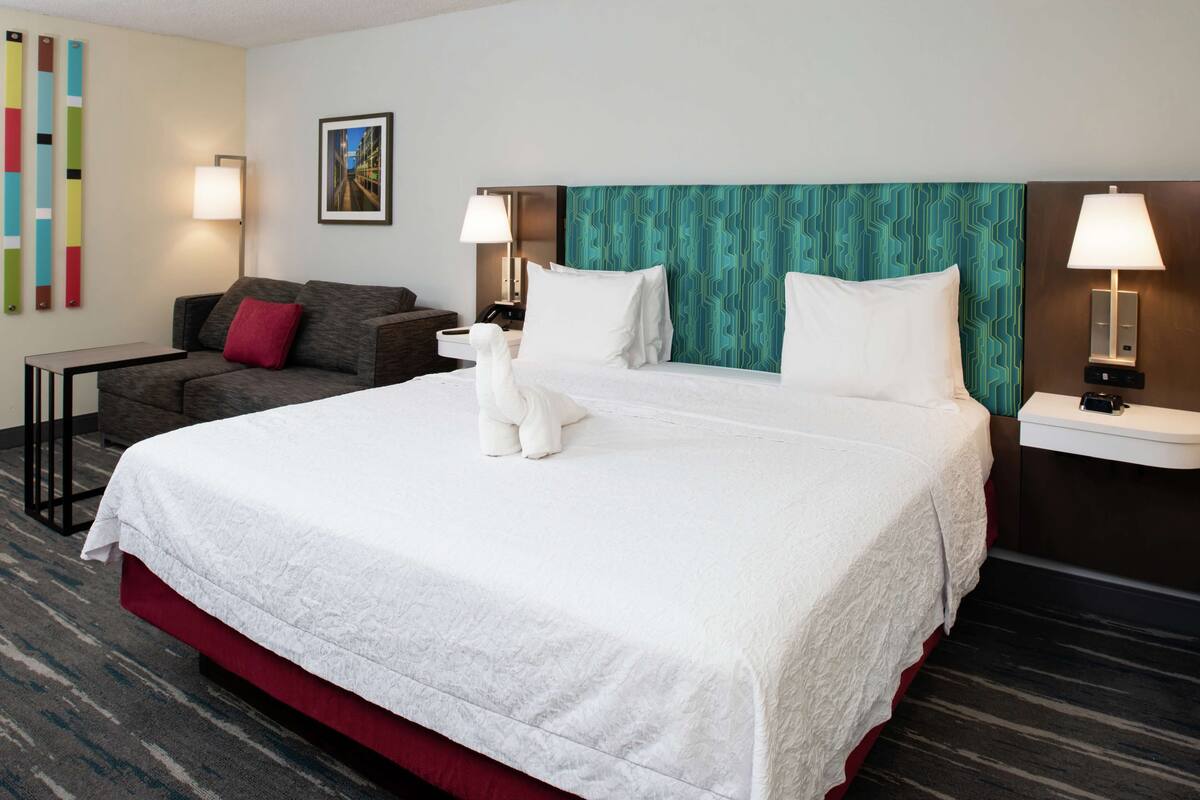 A hotel room with a large bed, a sofa, a desk, and a nightstand.