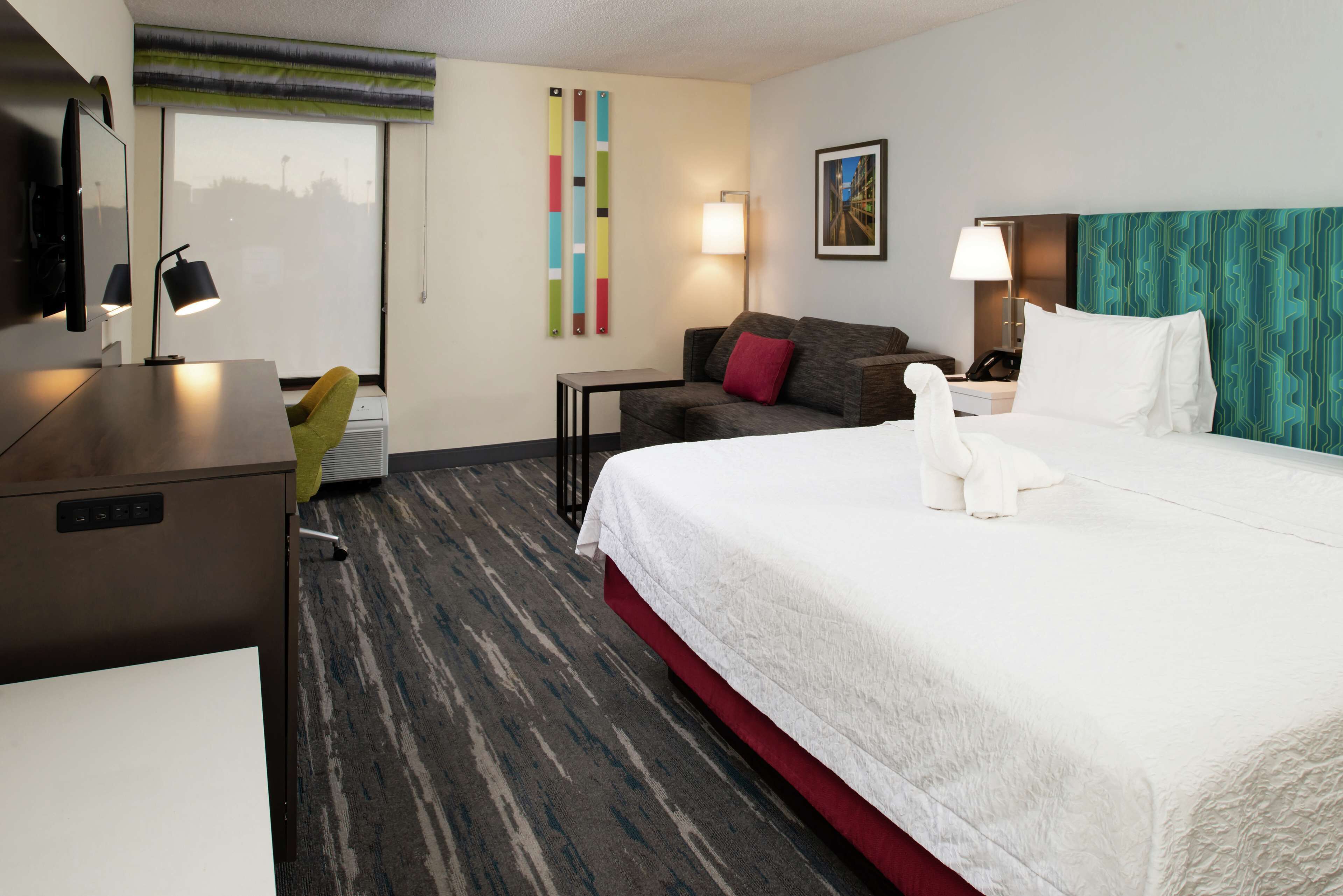 A hotel room with a large bed, a desk, a chair, a sofa, and a TV.
