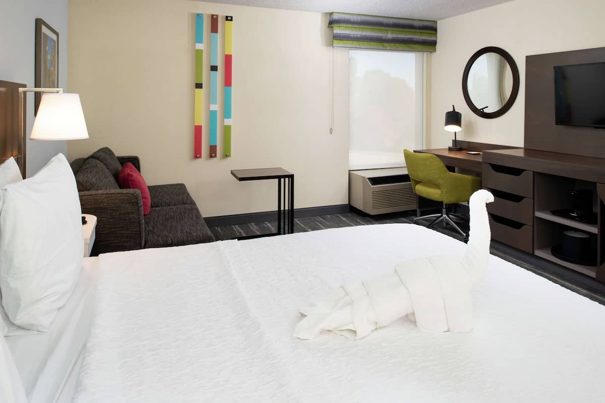 A hotel room with a bed, a desk, a chair, a TV, and a window with a view.