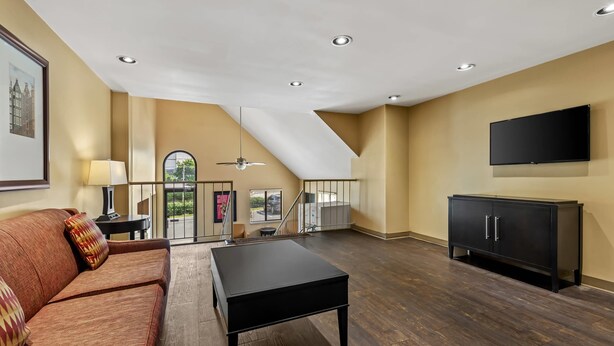 A spacious living room with a high ceiling, dark wooden flooring, a black sofa, a black coffee table, and a black cabinet.