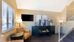 A hotel lobby with a seating area, a coffee station, a flat-screen TV, and a staircase.