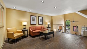 A spacious living area with a sofa, armchair, and coffee table, featuring wooden flooring and recessed ceiling lights.