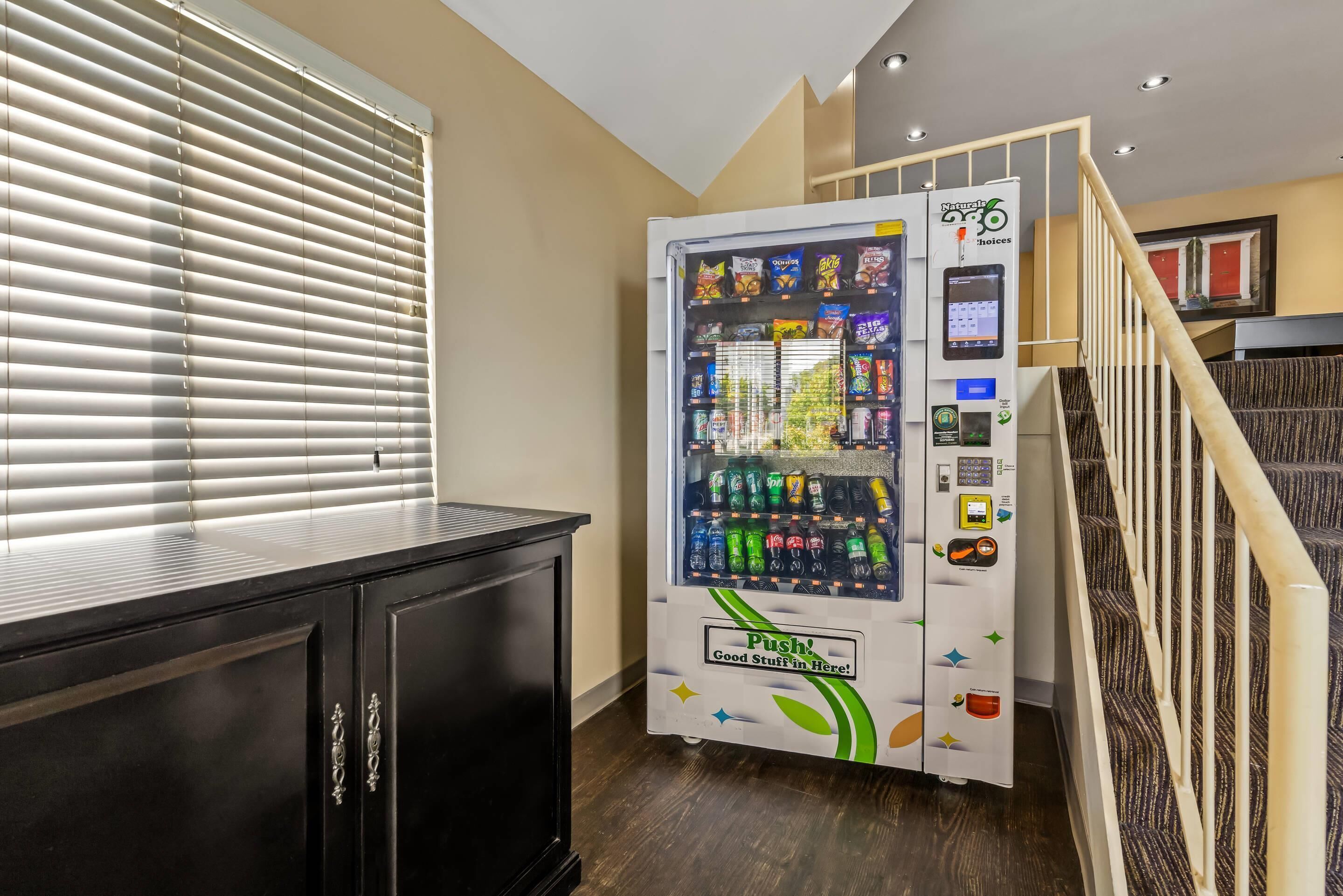 A vending machine with a variety of snacks and drinks, located in a hallway with a staircase.