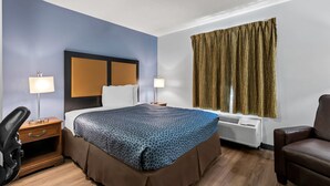 A hotel room with a bed, bedside lamps, a desk, a chair, and a window with curtains.