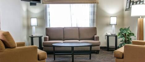 A living room with a sofa, two armchairs, a coffee table, a TV, and a window with curtains.