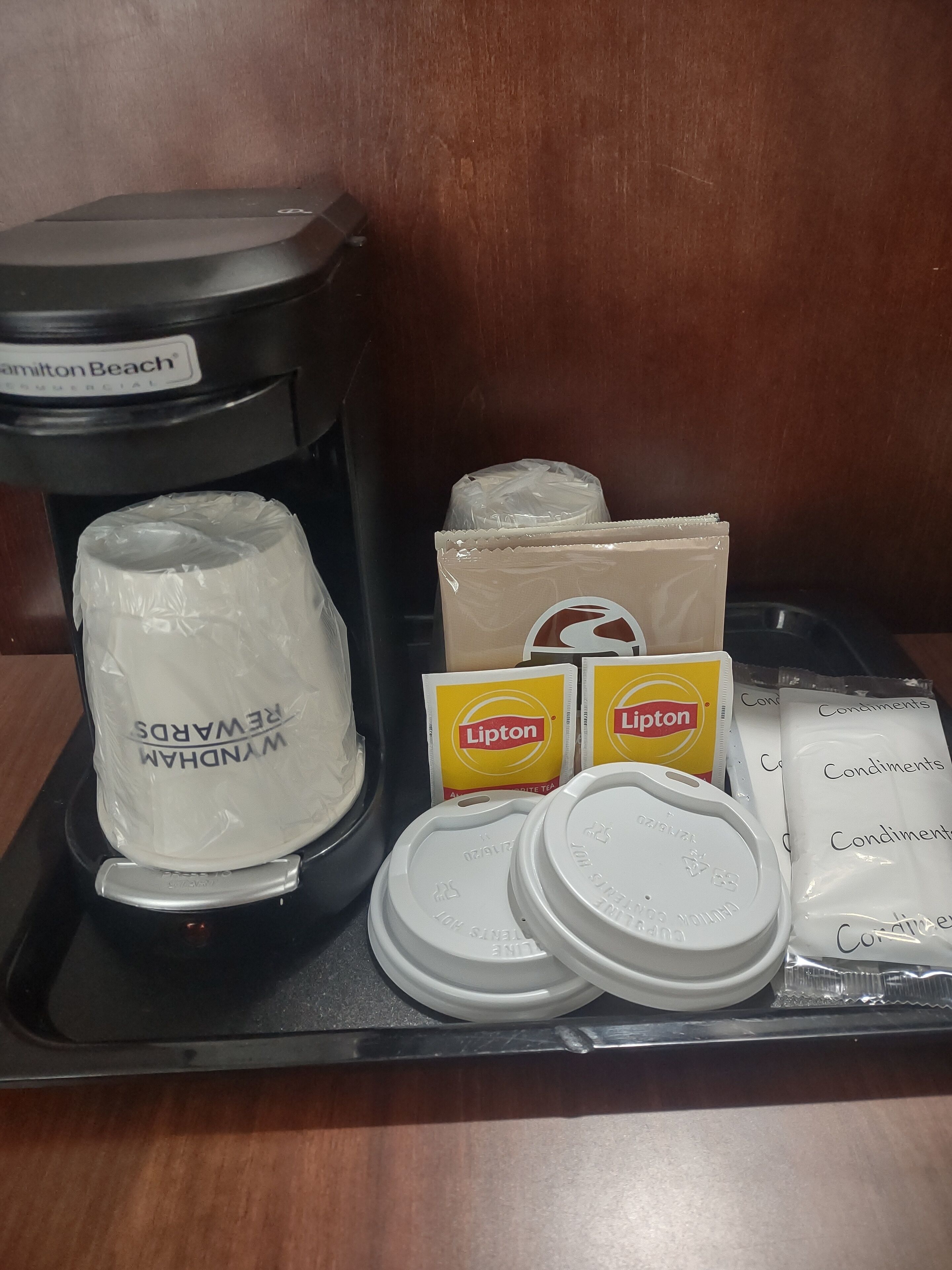A tray with a Hamilton Beach coffee maker, two Lipton tea packets, and several containers of condiments.