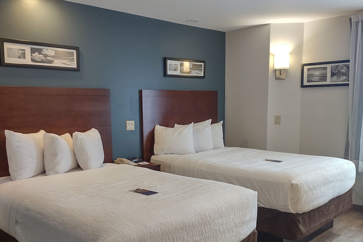 Duas camas de casal com cabeceiras de madeira, roupa de cama branca e uma parede de destaque azul.