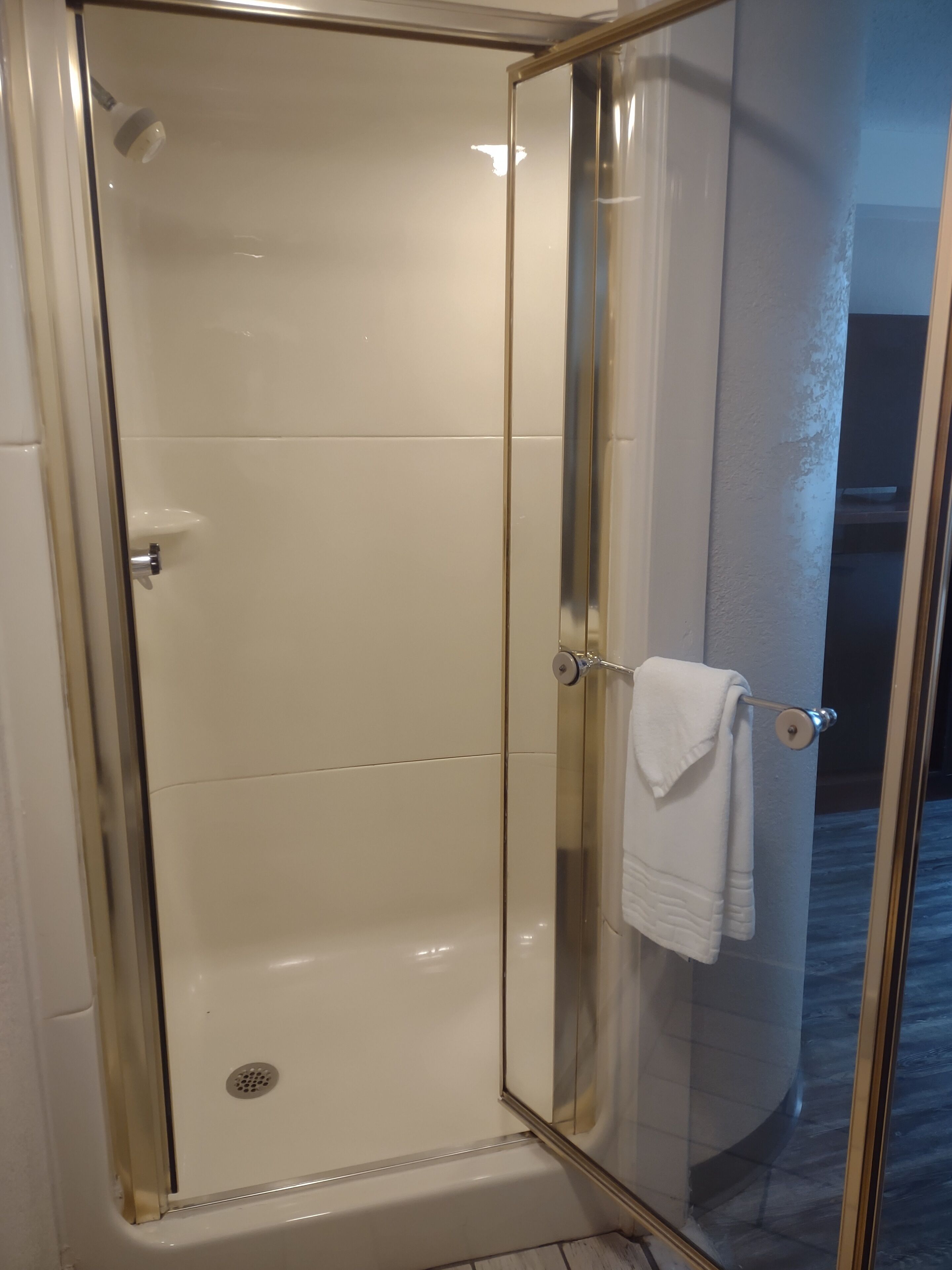 A glass-enclosed shower with a white tiled interior, a visible drain, and a towel hanging on the door handle.