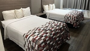 Twee bedden met witte lakens en een geruit plaid, een houten hoofdbord, een nachtkastje en een raam met gordijnen.