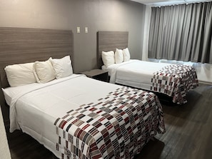 Deux lits avec du linge de lit blanc et une couverture à carreaux, une tête de lit en bois, une table de chevet et une fenêtre avec des rideaux.