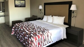 Hotelkamer met een groot bed, twee bedlampjes, een nachtkastje, een stoel, een bureau met een spiegel en een schilderij aan de muur.