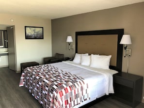 A hotel room with a large bed, two bedside lamps, a nightstand, a chair, a desk with a mirror, and a painting on the wall.