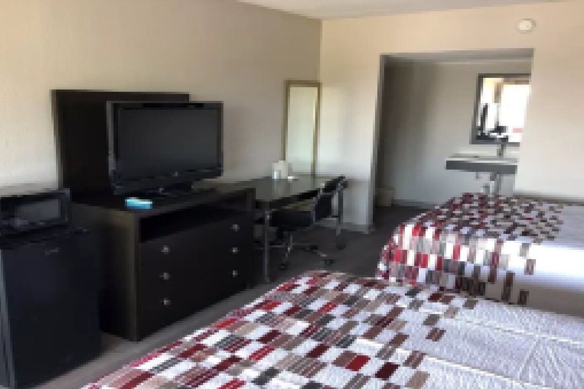 Una habitación de hotel con una cama, un escritorio con una computadora, una televisión y un aparador.