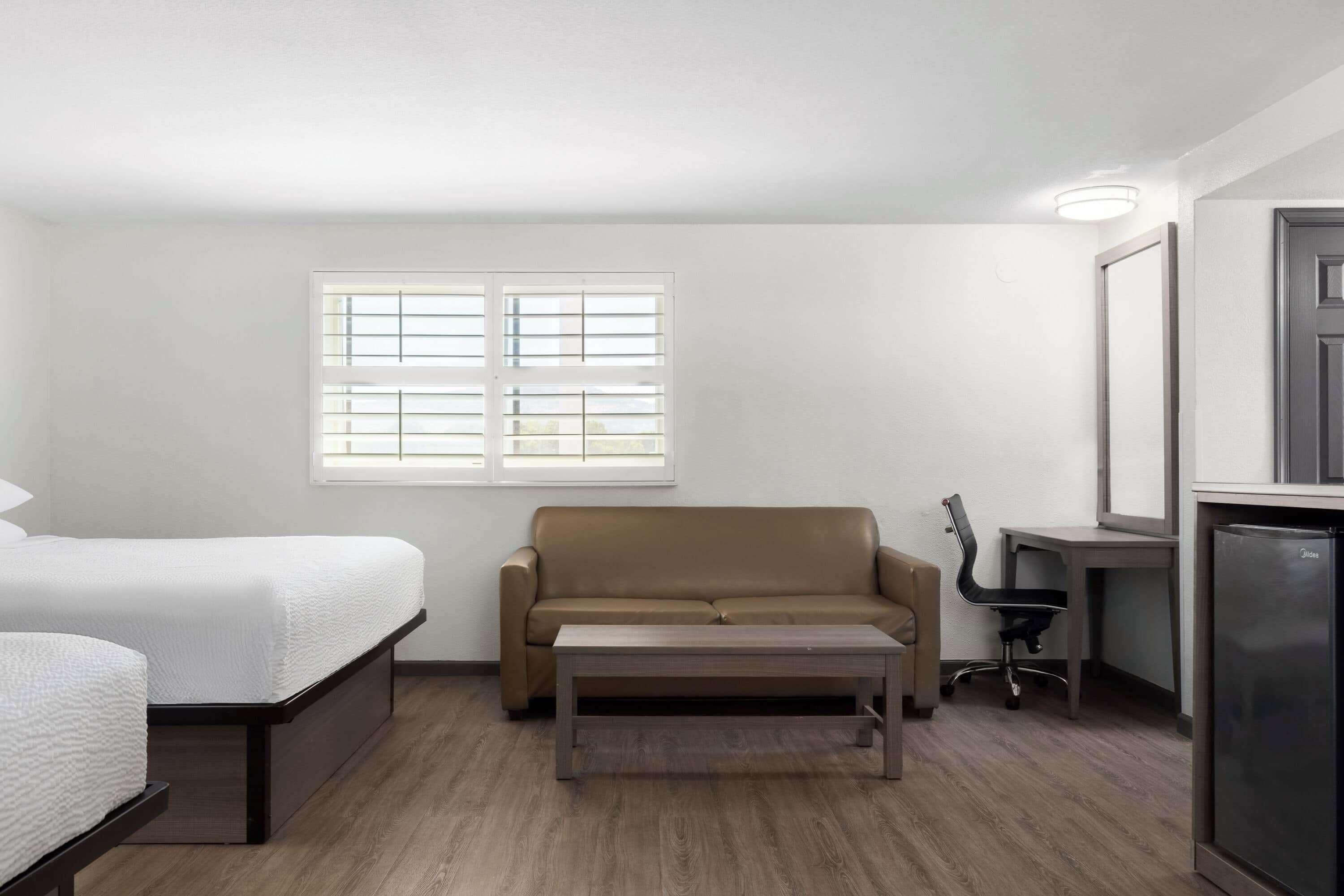 A compact hotel room with a bed, a sofa, a small table, a desk, and a refrigerator.