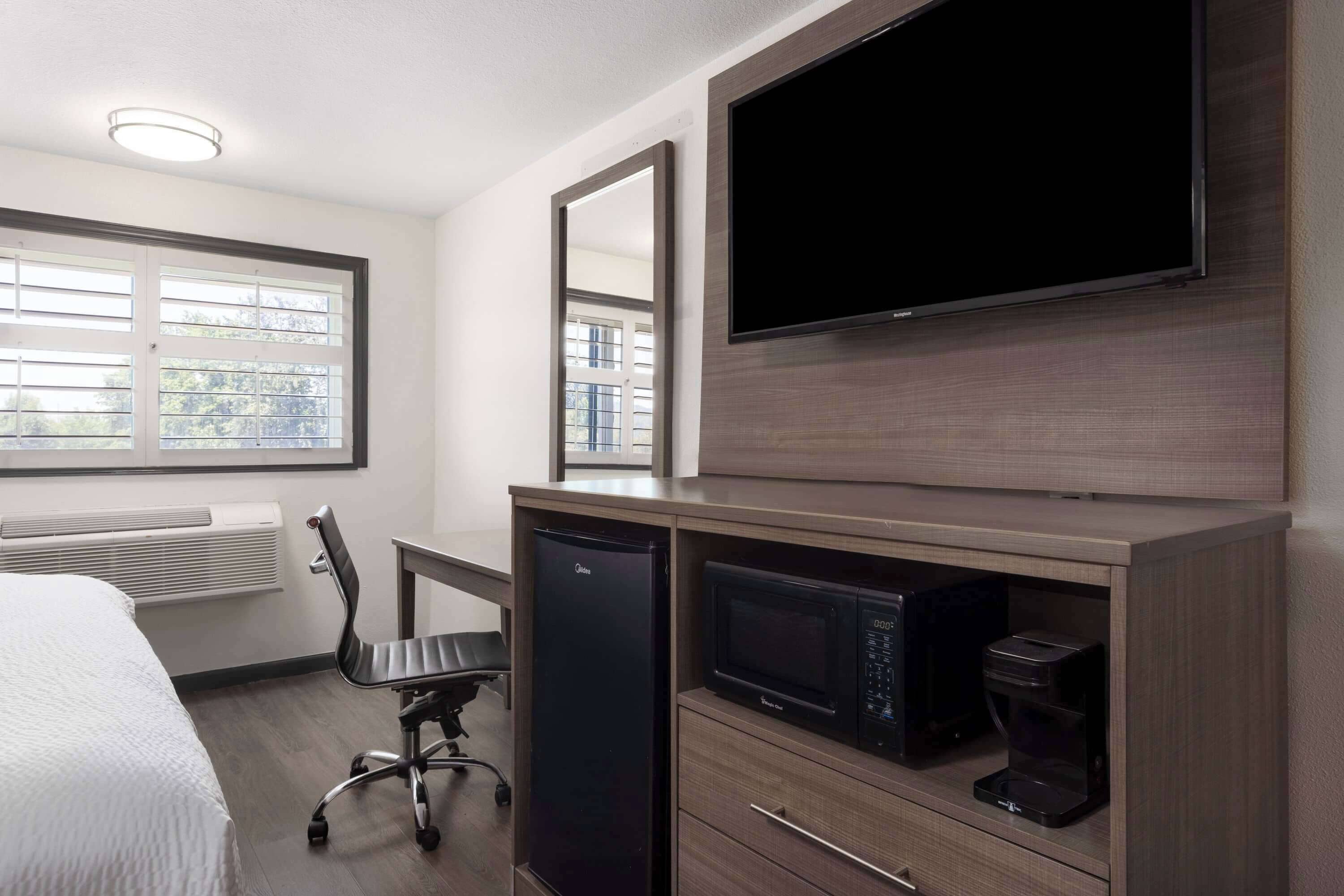 A hotel room with a bed, a desk with a chair, a flat-screen TV, a microwave, and a coffee maker.