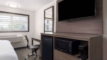 A hotel room with a bed, a desk with a chair, a flat-screen TV, a microwave, and a coffee maker.