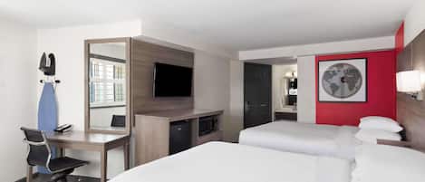A hotel room with a desk, two beds, a TV, a mirror, and a world map on the wall.