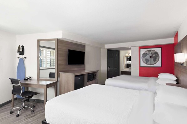 A hotel room with a desk, two beds, a TV, a mirror, and a world map on the wall.
