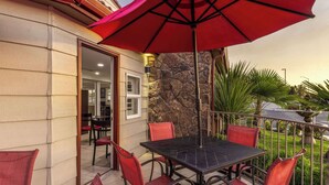 An outdoor patio with a table and chairs, a red umbrella, and a stone wall.