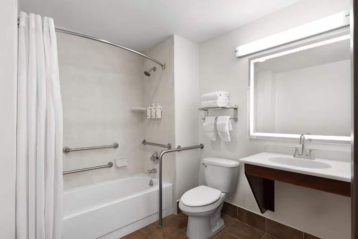 Ein Badezimmer mit Badewanne, Toilette und Waschbecken, ausgestattet mit Haltegriffen und einer Duschvorhang.