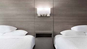 Una habitación de hotel con dos camas, una mesita de noche y una lámpara fijada a la pared.