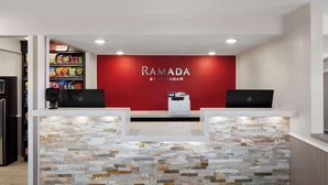 A reception area with a stone wall and a red wall displaying the name 'RAMADA BY WYNDHAM'.