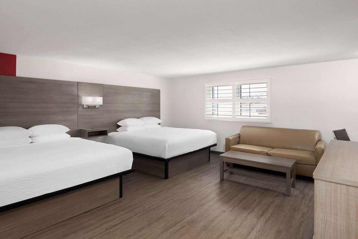 Ein modernes Hotelzimmer mit zwei Betten, einem Schlafsofa, einem Couchtisch und einem Fenster mit Jalousien.