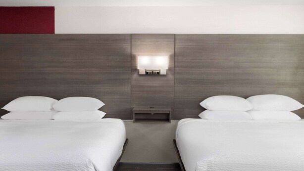 A hotel room with two beds, a nightstand, and a wall-mounted light fixture.