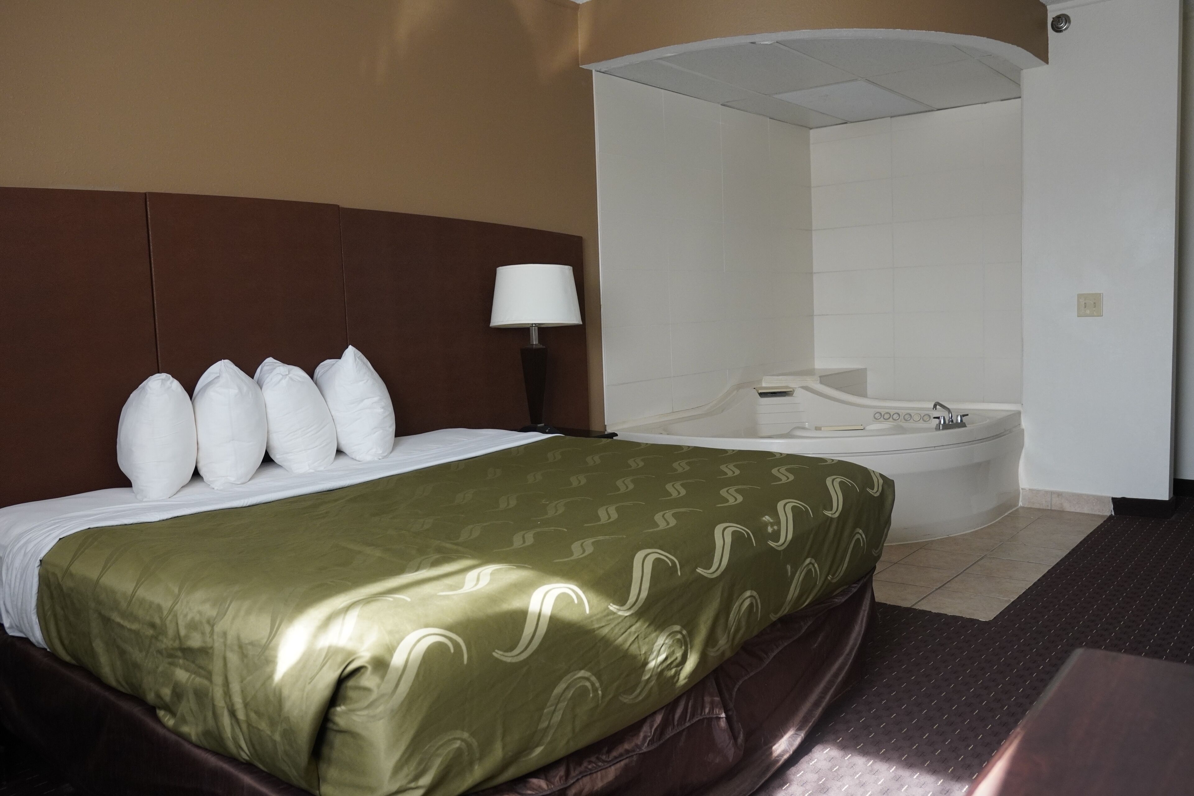 A hotel room with a bed, a headboard, a lamp, and a bathtub.