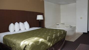 A hotel room with a bed, a headboard, a lamp, and a bathtub.