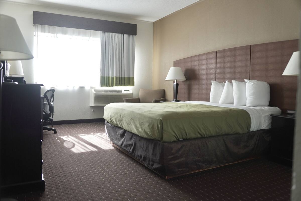 A hotel room with a large bed, two bedside lamps, a desk with a chair, and a window with curtains.