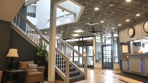 A lobby with a staircase, a reception desk, and a clock. - American Inn & Suites Waterford (Waterford)