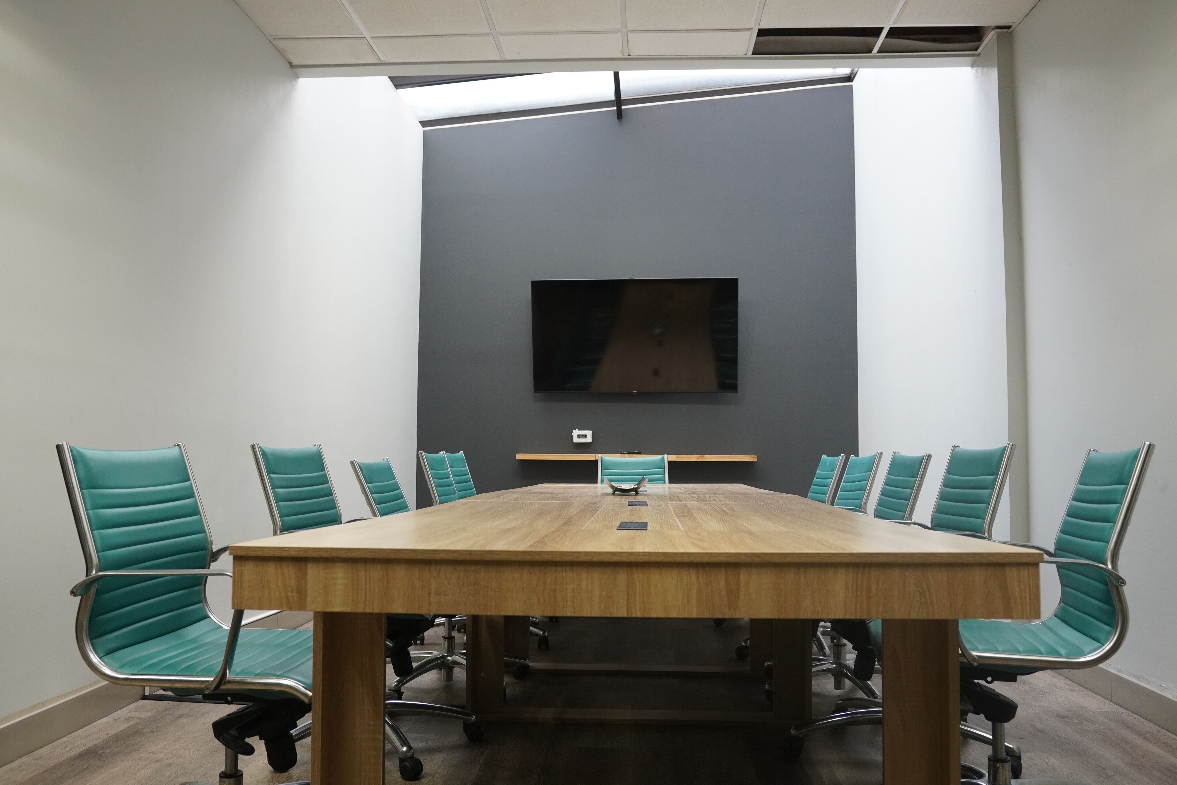 Un salón de conferencias con una gran mesa de madera, sillas tapizadas en verde y un televisor de pantalla plana montado en la pared.