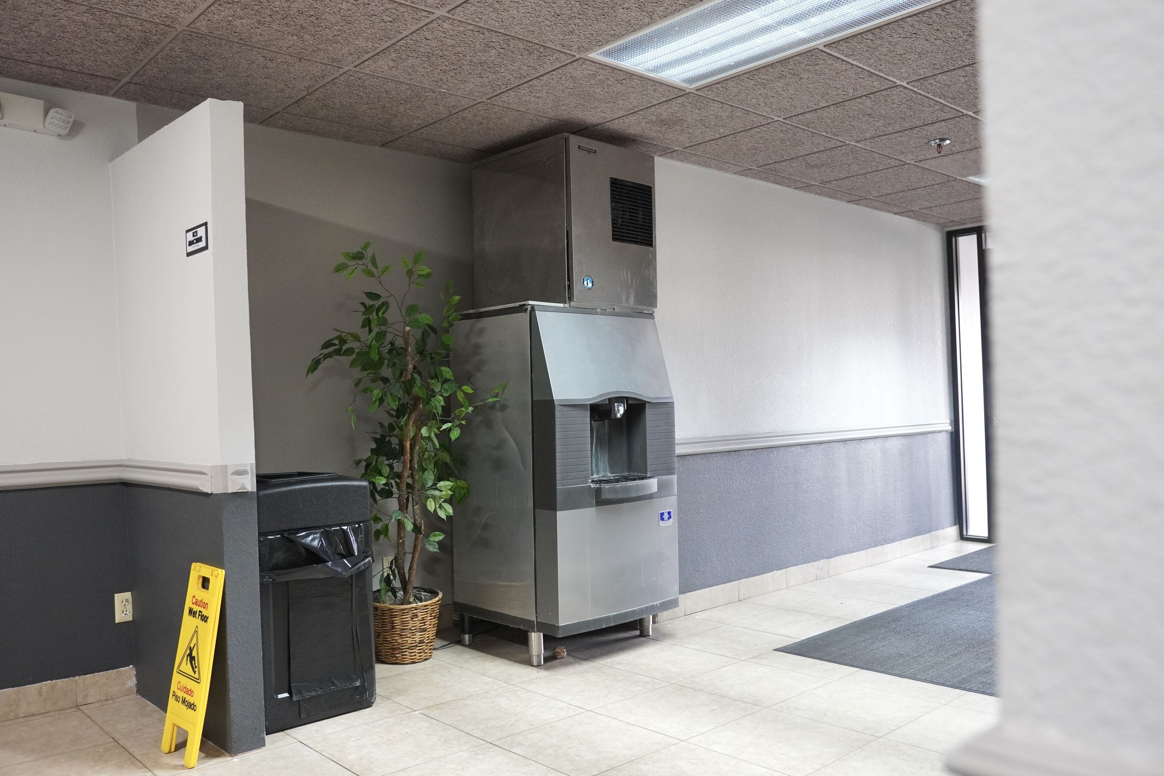 A clean, modern lobby with a water dispenser, trash bin, and a caution sign near the entrance.