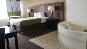 A hotel room with a bed, two bedside lamps, a large bathtub, and a desk. - American Inn & Suites Waterford (Waterford)