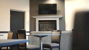 A conference room with a fireplace, a flat-screen TV mounted above it, and a table with chairs. - American Inn & Suites Waterford (Waterford)