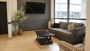 A modern living room with a sofa, a coffee table, and a large window offering a view of the outside. - American Inn & Suites Waterford (Waterford)
