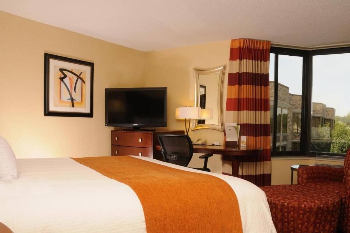 A hotel room with a bed, television, desk, chair, and large window.