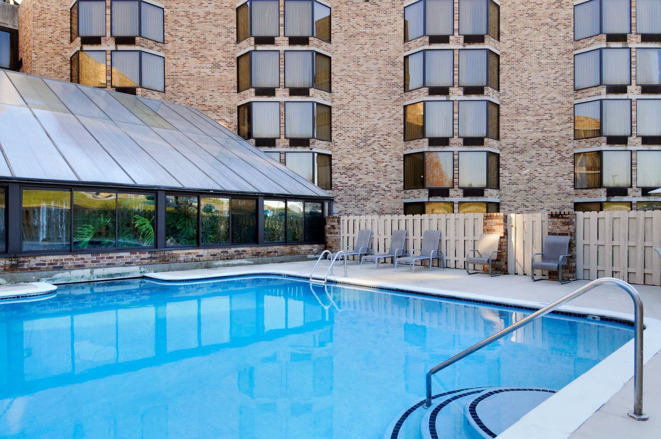 A swimming pool with a metal roof and a brick building with multiple windows in the background.